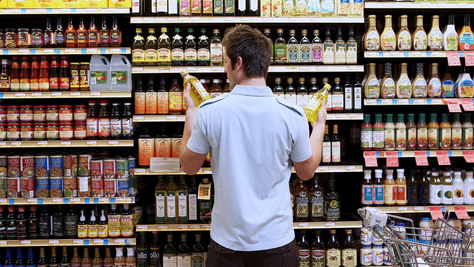 man comparing olive oil at grocery store