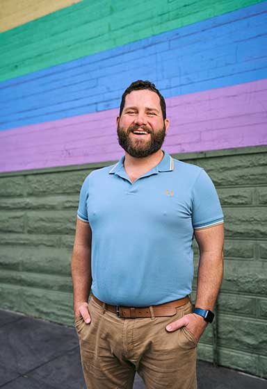 Brian Redmond standing in front of a wall painted with rainbow colors