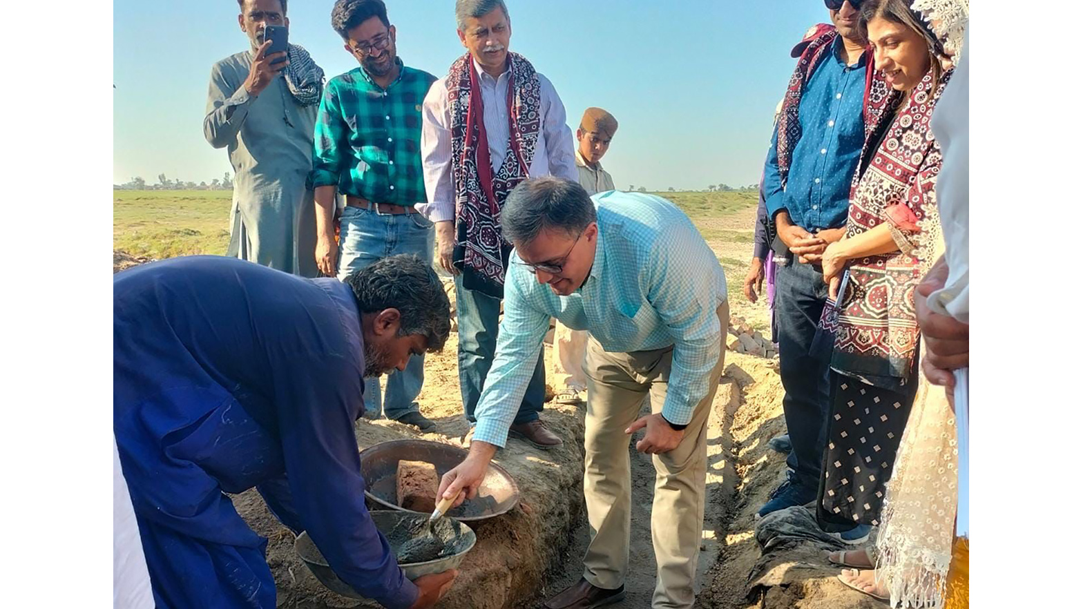 Ahmed Zaheer, country chairman and general manager of Chevron Pakistan, lays clay on the foundation of a new home as locals who lost their possessions during historic flooding stand by.