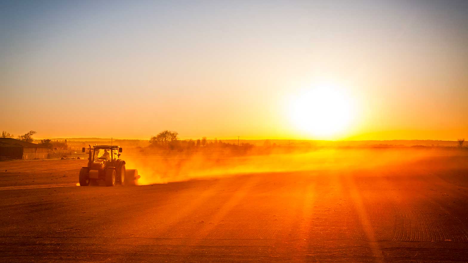 image of a farm tractor driving as the sun is setting over the fields