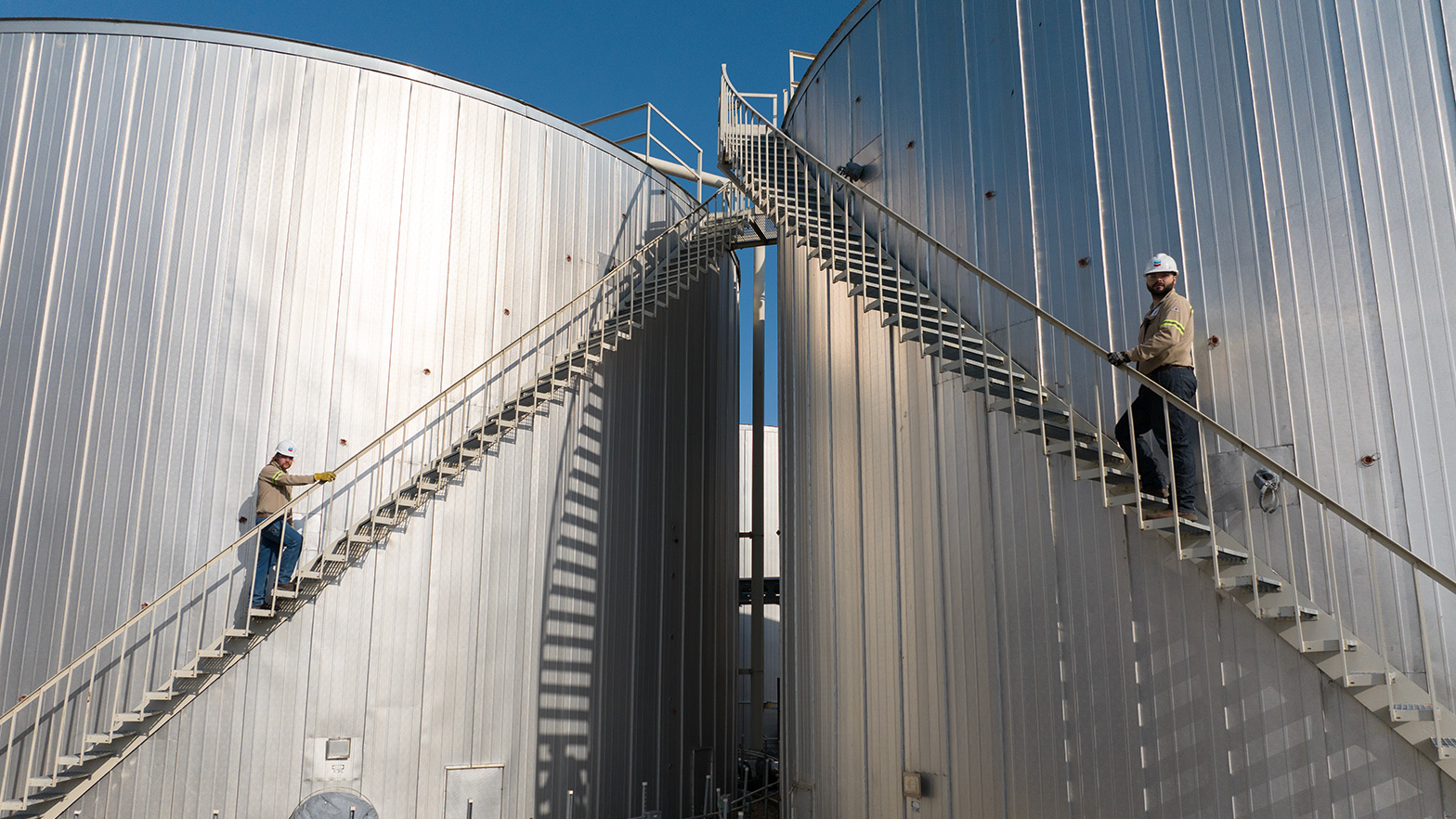 Workers climbing up stairs to the top of two stage tanks at a Chevron Renewable Energy Group biorefinery.