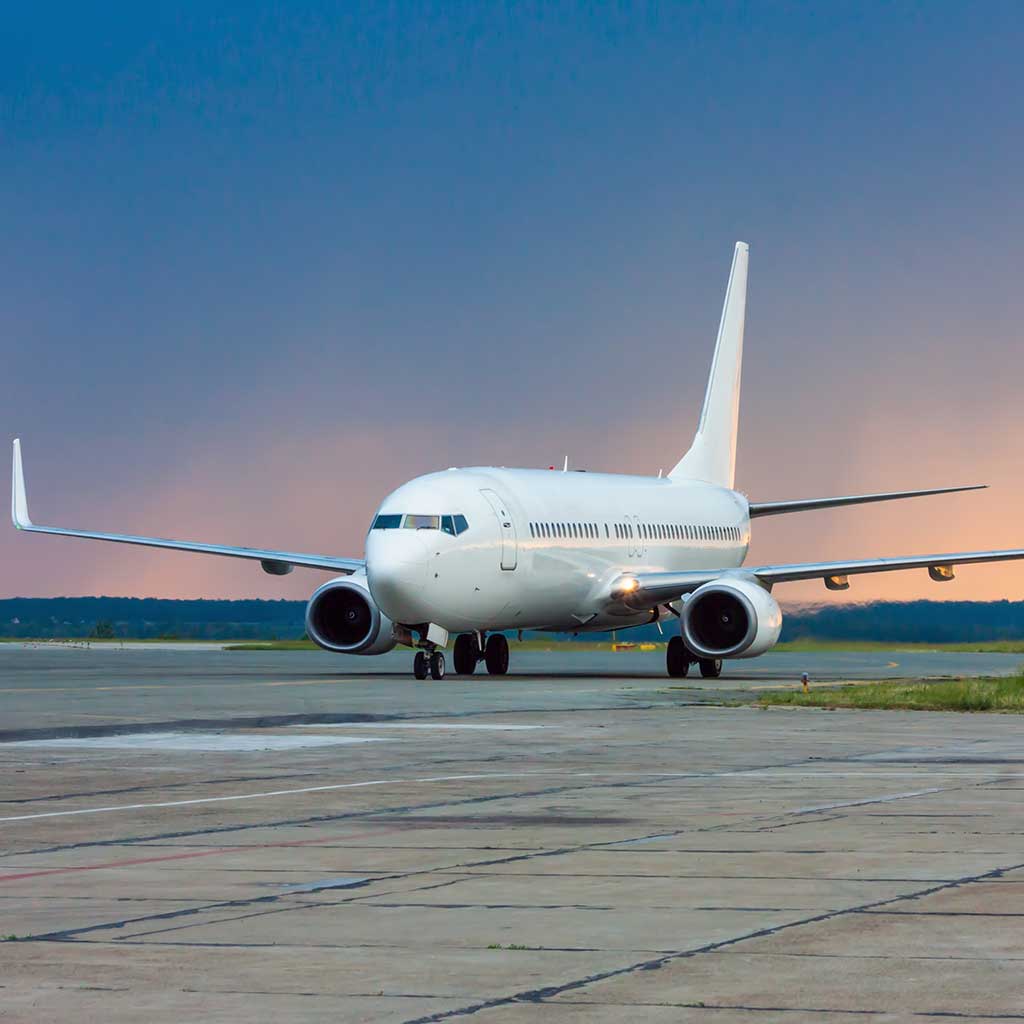 A jetliner taxis on the main airport runway at sunrise. Rain clouds are seen in the background
