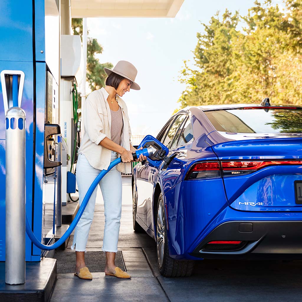 A woman fills her car with hydrogen at a fueling station