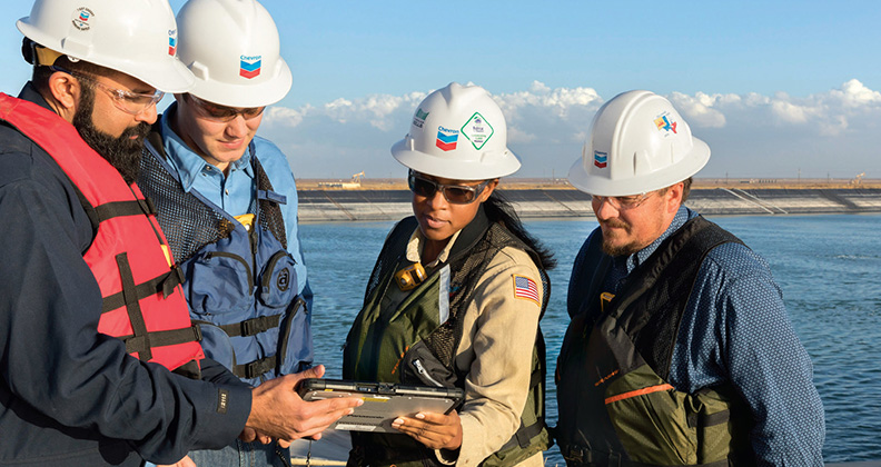 Four Chevron employees wearing hard hats at water's edge.