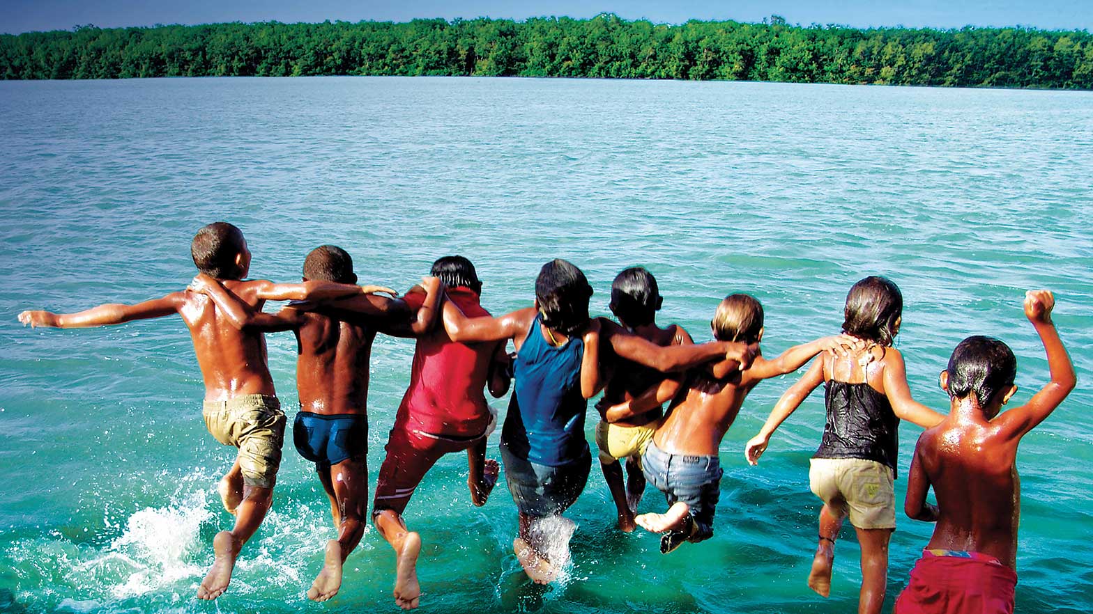 a group of children lock hands and jump into the water together